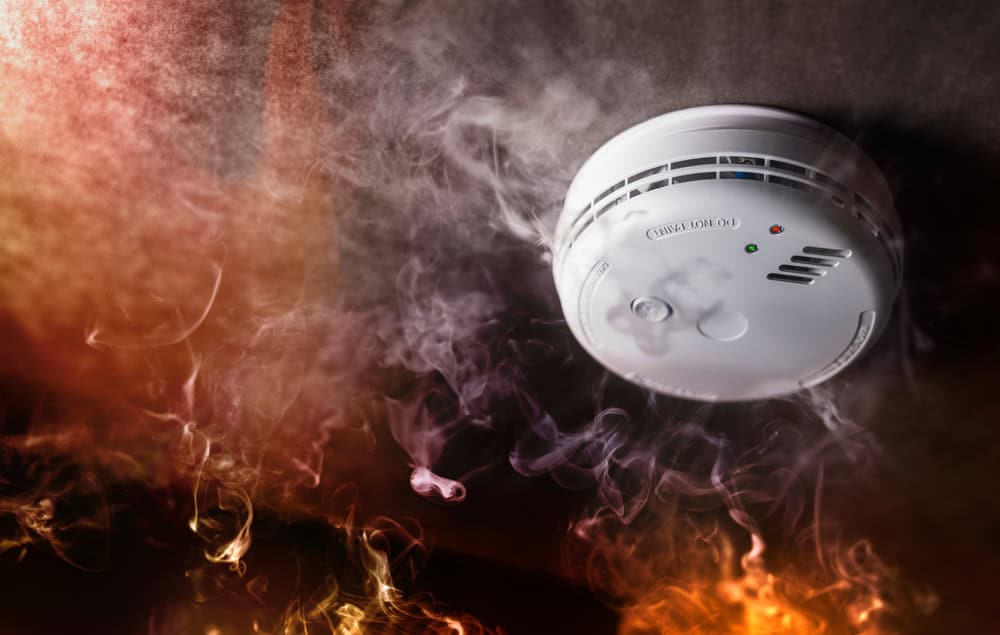 A smoke detector stands vigilant amidst swirling smoke and flames, ready to alert in case of fire.