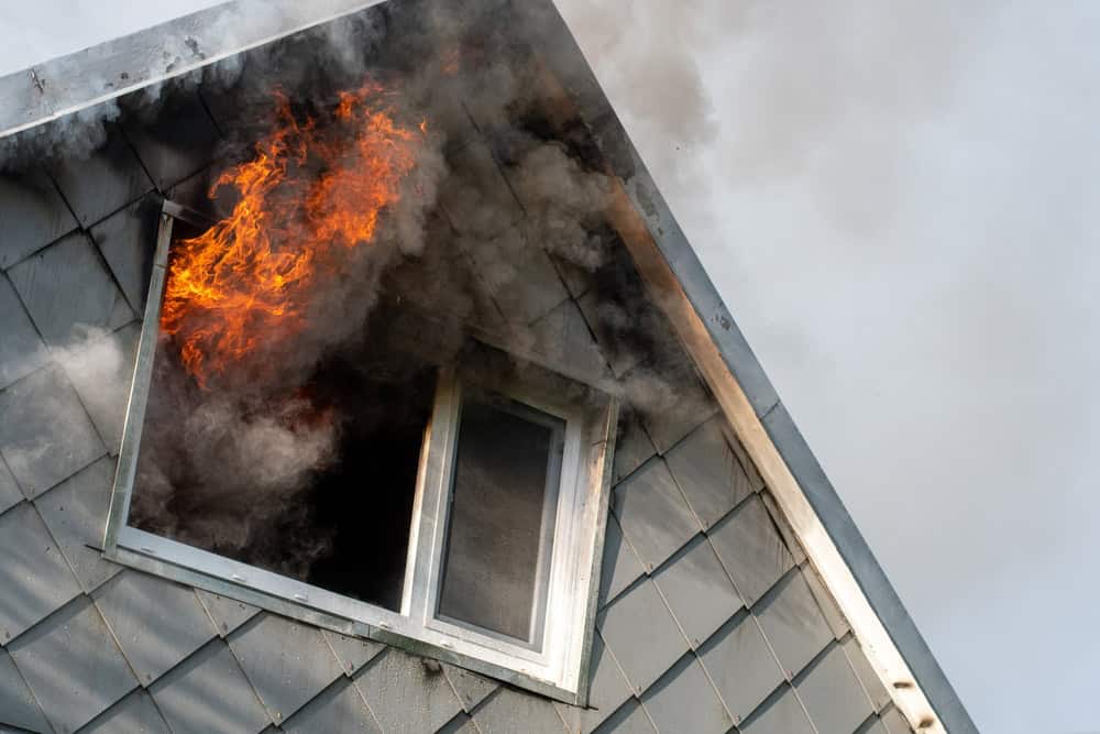 A house engulfed in flames, with fire bursting through a window.