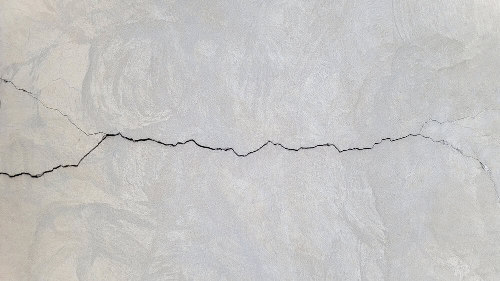 A stark, black crack disrupts the smooth, pale surface of a wall, hinting at underlying tensions.