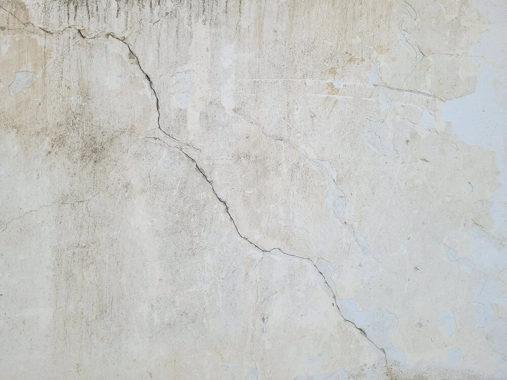 Cracks and peeling paint reveal the passage of time on this weathered wall.
