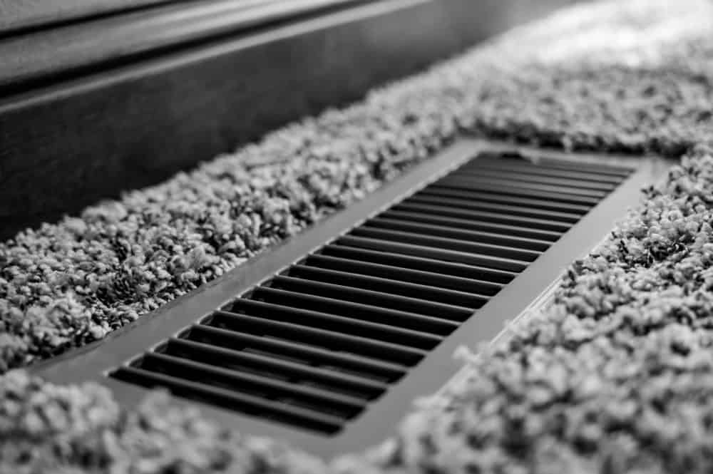 A cozy carpet meets a sleek floor vent in this monochrome close-up.