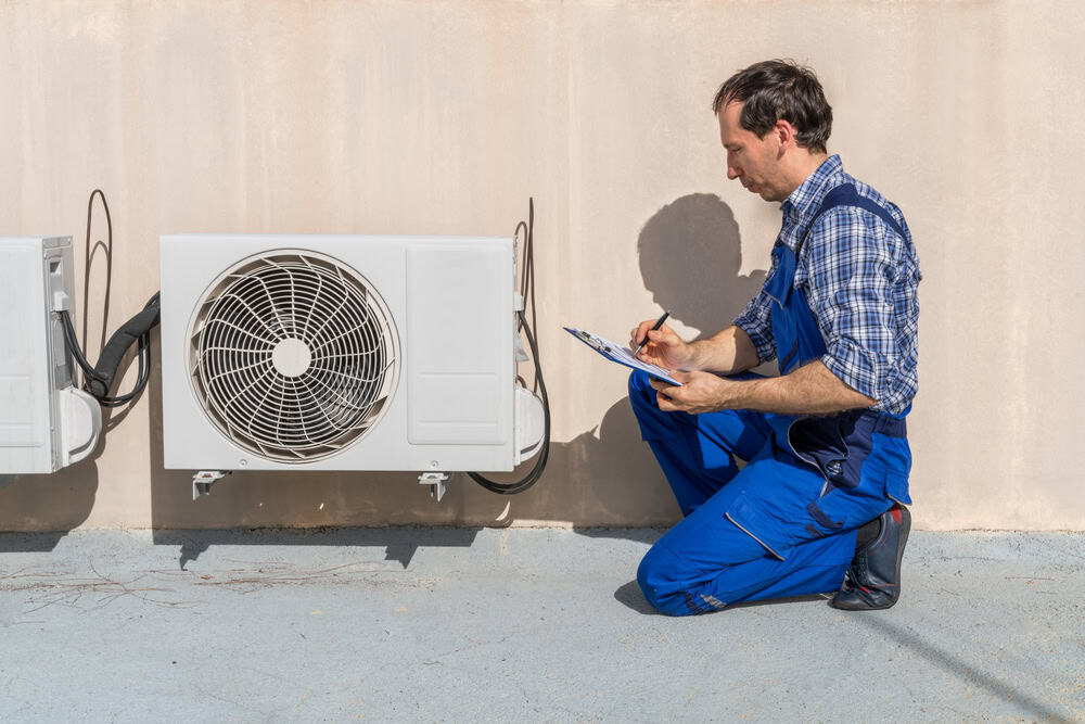 An HVAC technician inspects and takes notes on an outdoor air conditioning unit.