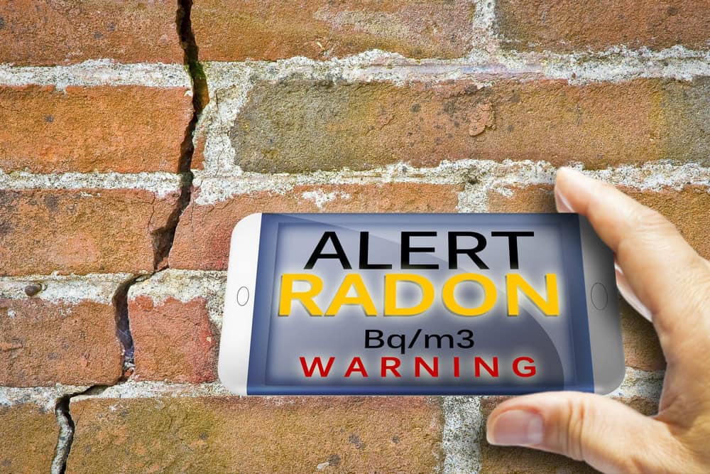 Radon alert on a phone screen held against a cracked brick wall.