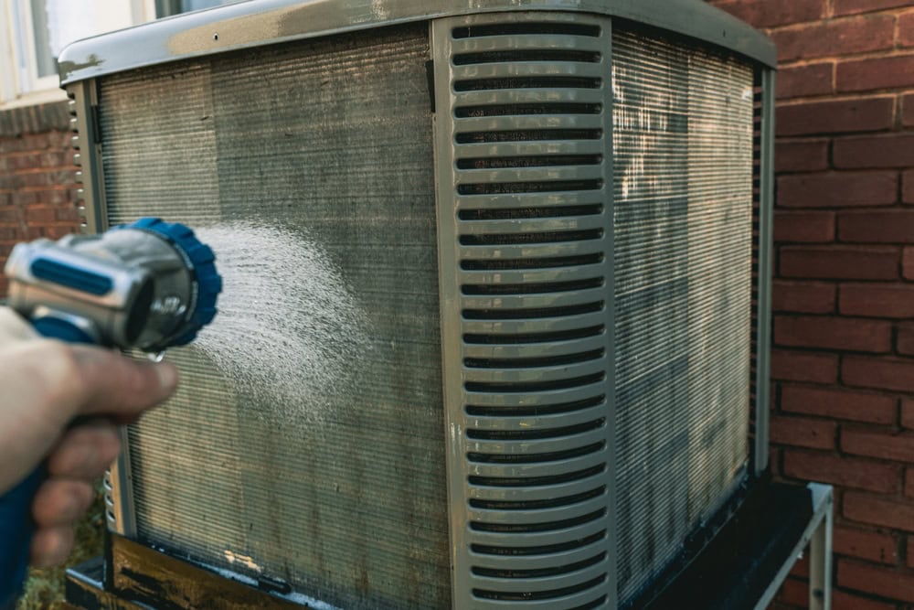 Cleaning the air conditioner with a power washer to ensure efficient cooling.