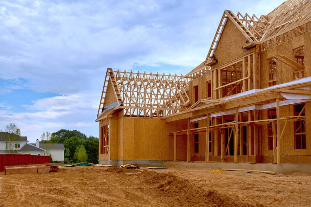 A new home under construction with intricate wooden framing against a bright blue sky.