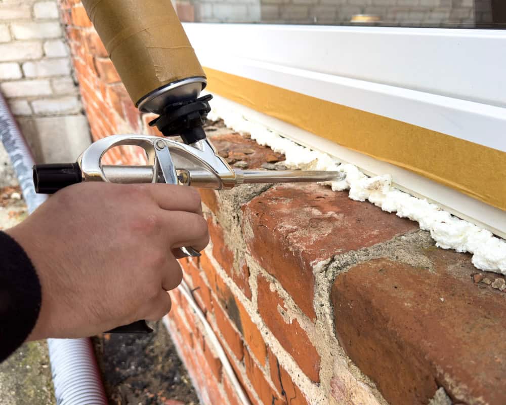 Applying foam sealant around a window frame for a secure installation.