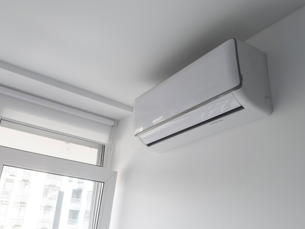 A sleek air conditioner unit mounted on a wall next to a bright window, providing cool comfort in a modern space.