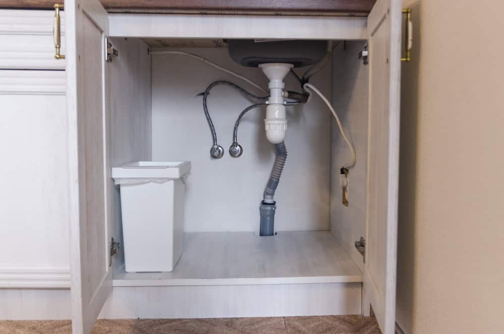 Under the sink: a tidy storage space with plumbing essentials and a trash bin.