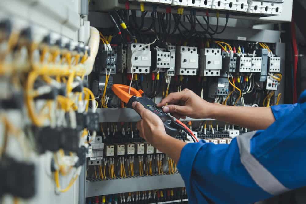 An electrician meticulously tests the voltage in a complex control panel, ensuring safety and efficiency.