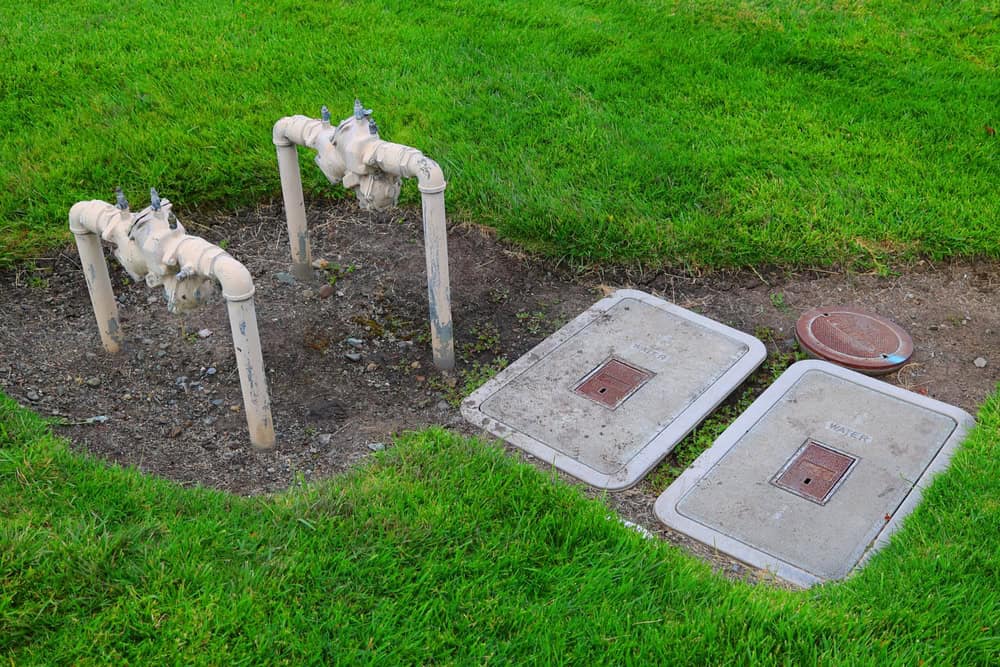 Utility access point with exposed irrigation pipes, surrounded by lush green grass.