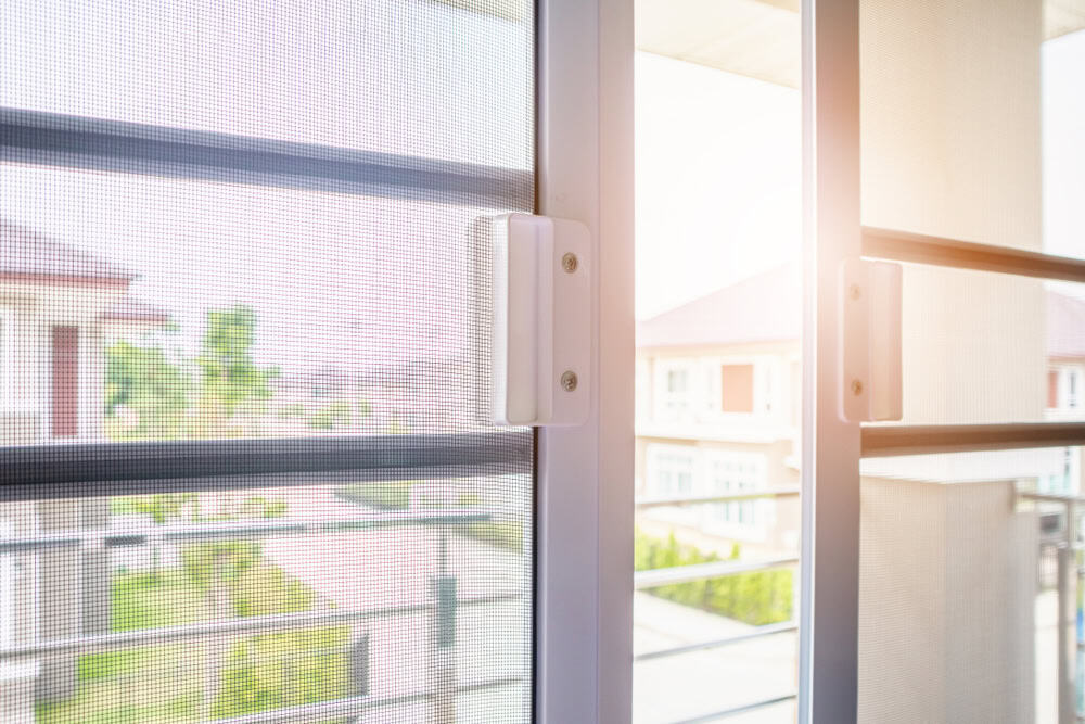 Sunlight streaming through a window with a mesh screen, offering a serene view of a residential neighborhood.