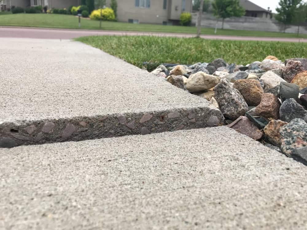 A close-up of a cracked concrete sidewalk bordered by a bed of colorful rocks.
