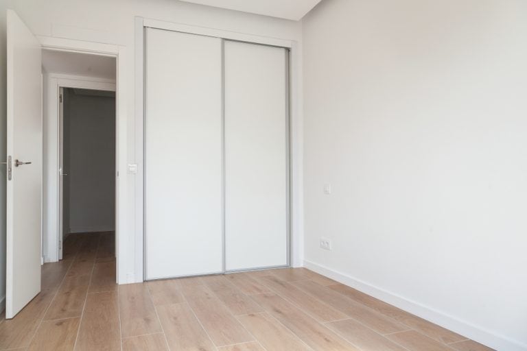 Bright and minimalistic empty room with wooden flooring and a built-in sliding wardrobe.