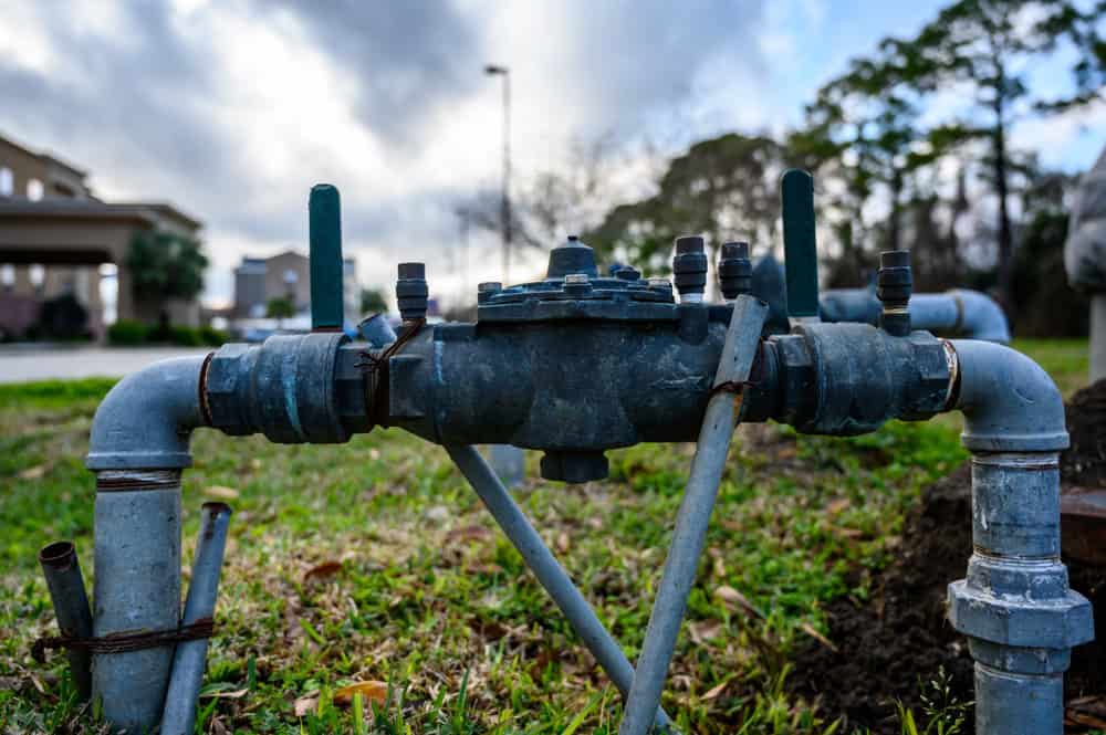 Rusty valves and pipes stand resilient amidst the green grass, under a cloudy sky.