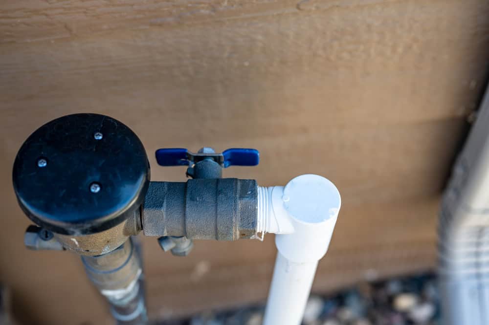 Outdoor water valve and PVC pipe connection against a wooden wall.