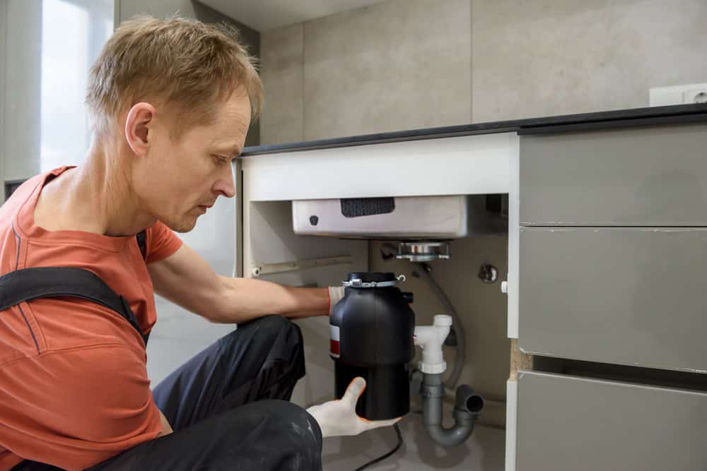 A plumber installs a garbage disposal under a kitchen sink, ensuring a smooth and efficient kitchen setup.