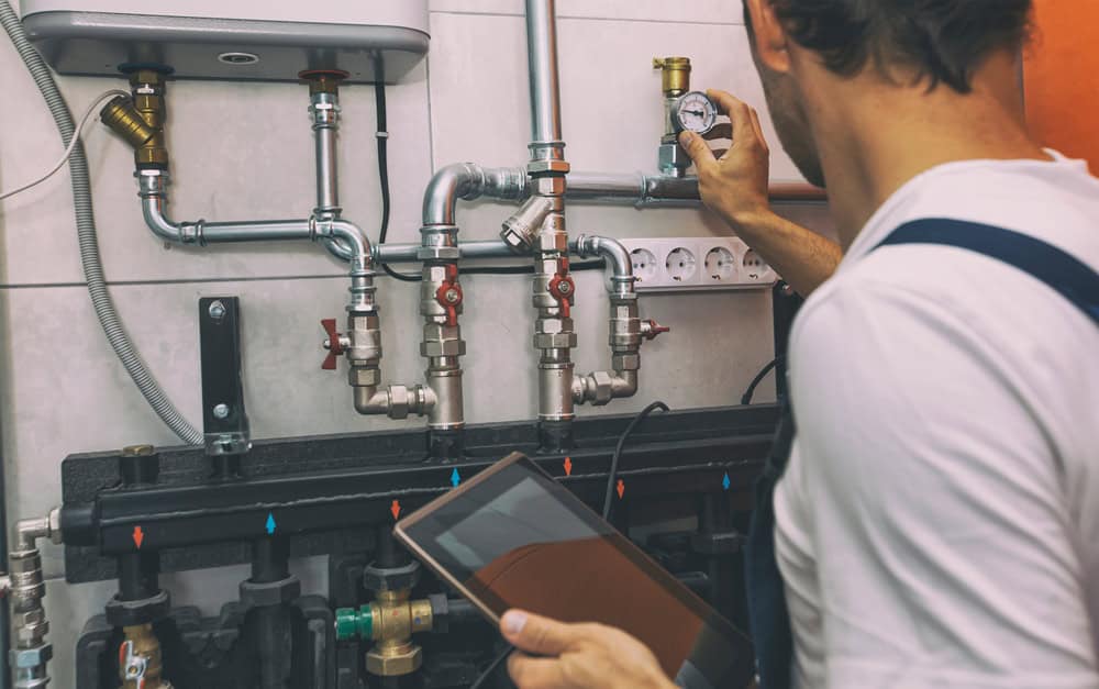 A technician uses a tablet to inspect and adjust the plumbing system in a modern utility room.