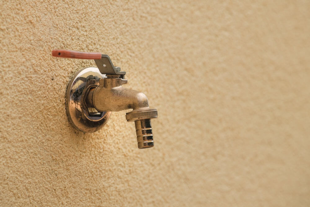 A rustic brass spigot with a red handle, mounted on a textured beige wall.