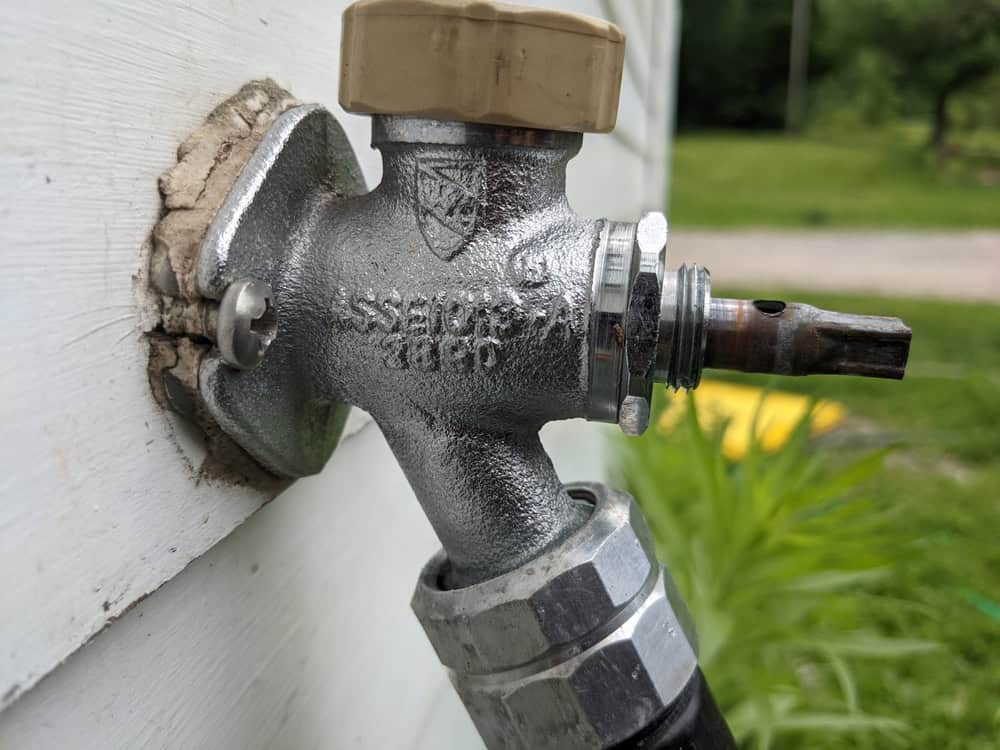 A close-up of an old, weathered outdoor faucet with the words "ZURN" and "1969" engraved, surrounded by lush greenery.