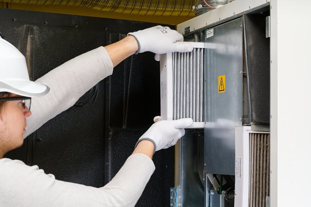 A technician carefully removes an air filter from an HVAC system for maintenance.