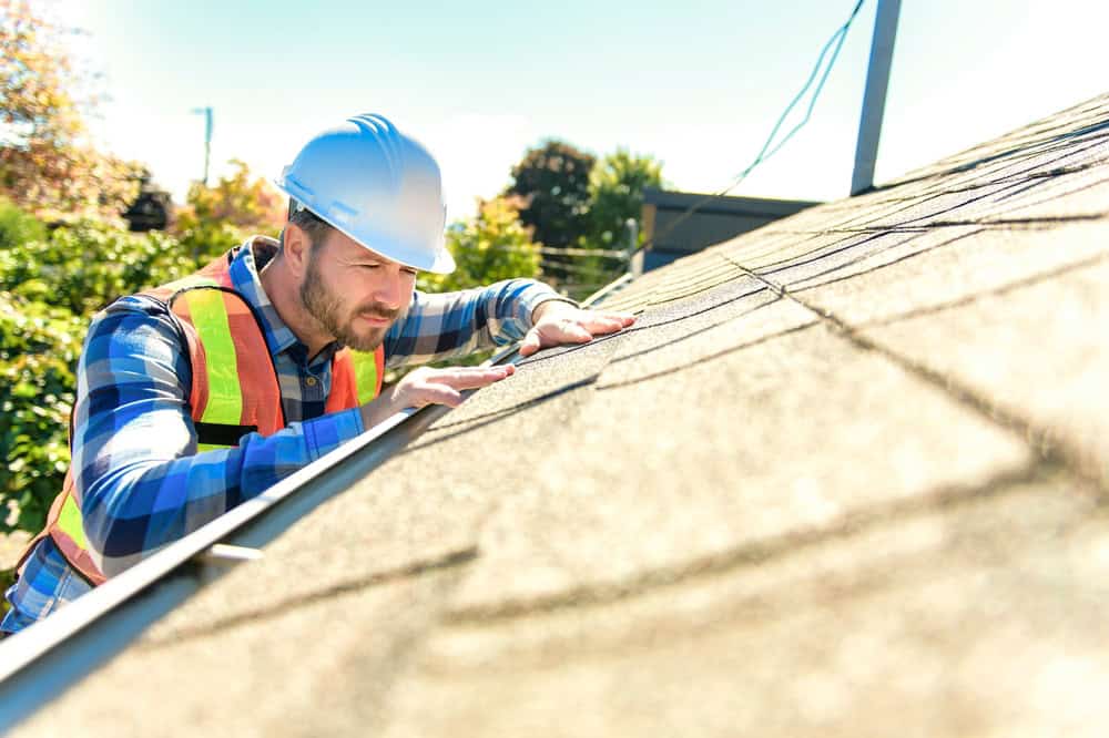 A roofer carefully inspects shingles on a sunny day.