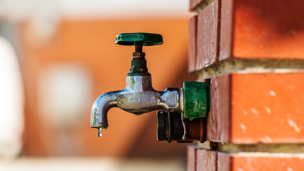 A dripping faucet attached to a brick wall, highlighting water conservation concerns.