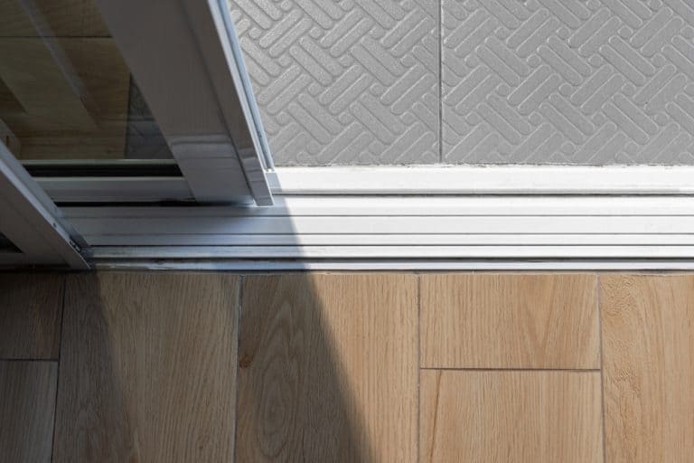 Sunlight streaming through an open sliding door, bridging warm wooden flooring and cool patterned tiles.