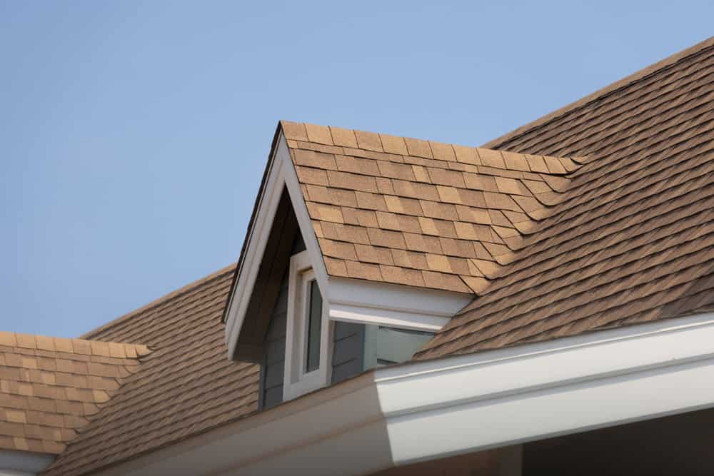 A cozy dormer window peeks out from a beautifully shingled roof under a clear blue sky.