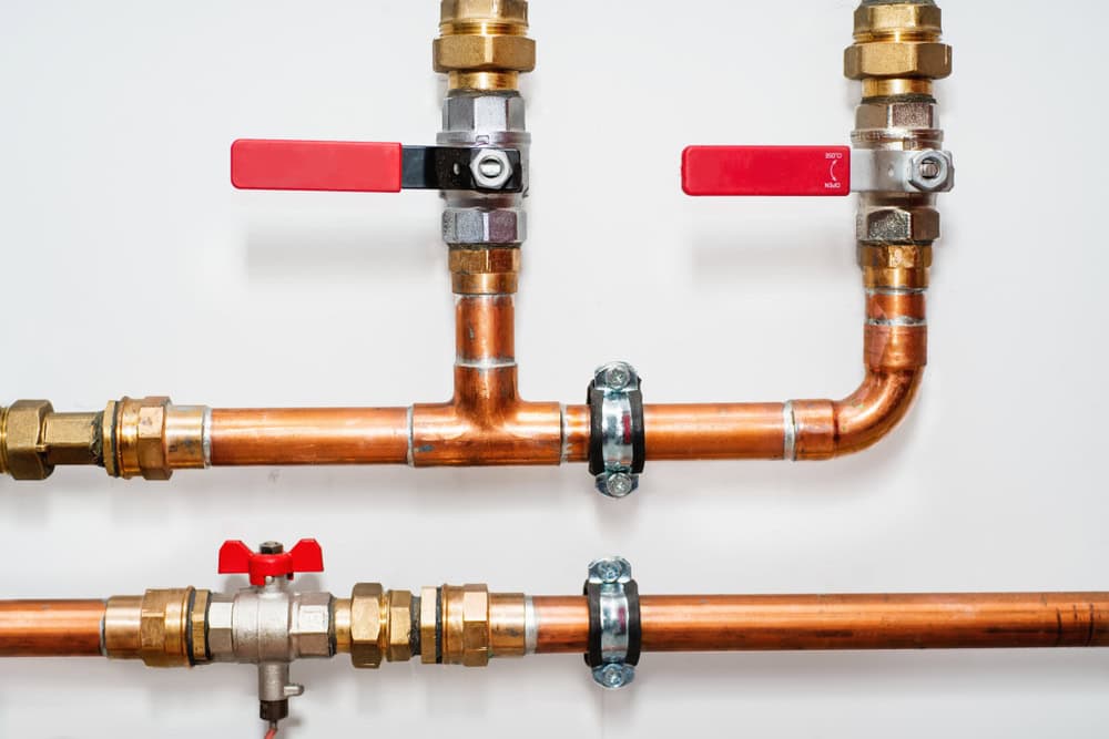Copper pipes with red-handled ball valves and brass fittings, ready for plumbing action.