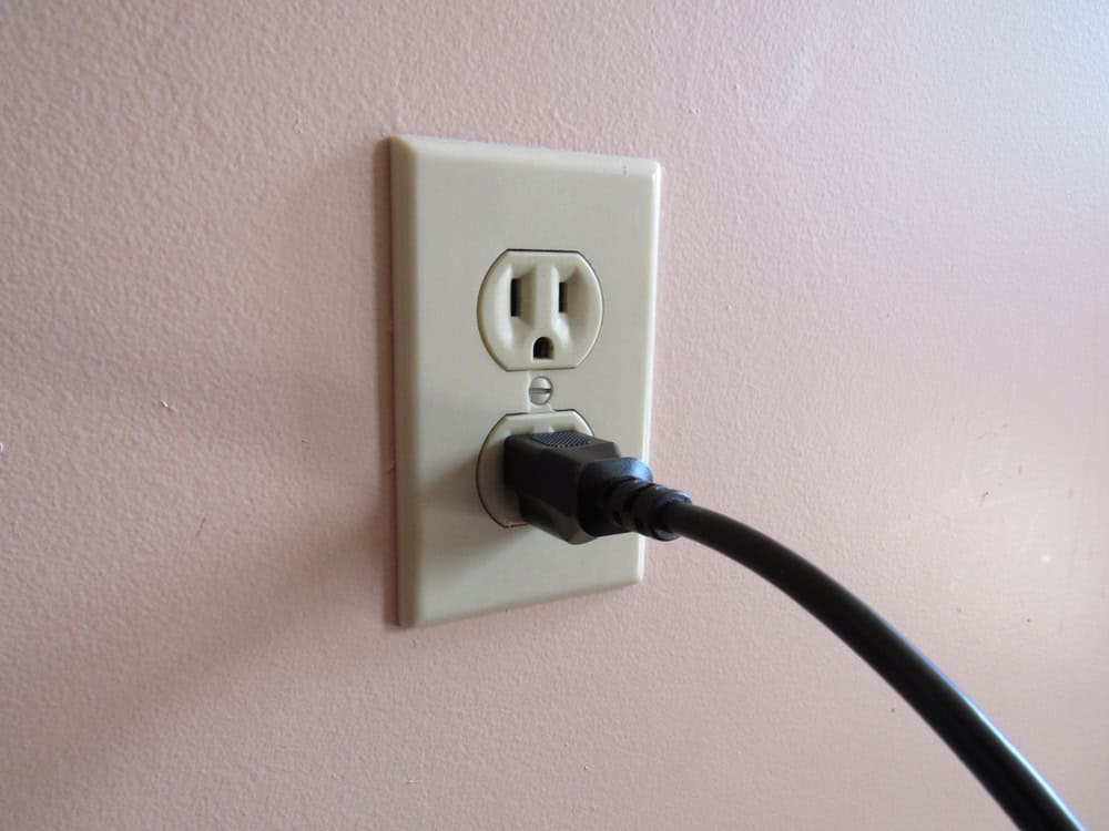 Powering up: A black plug connects to a standard wall outlet on a soft pink wall.