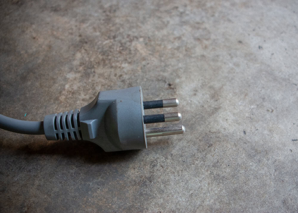 A close-up of a three-pin electrical plug resting on a textured concrete surface.