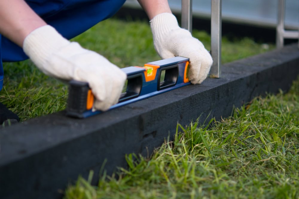 A gardener uses a spirit level to ensure a perfect alignment on a garden border.