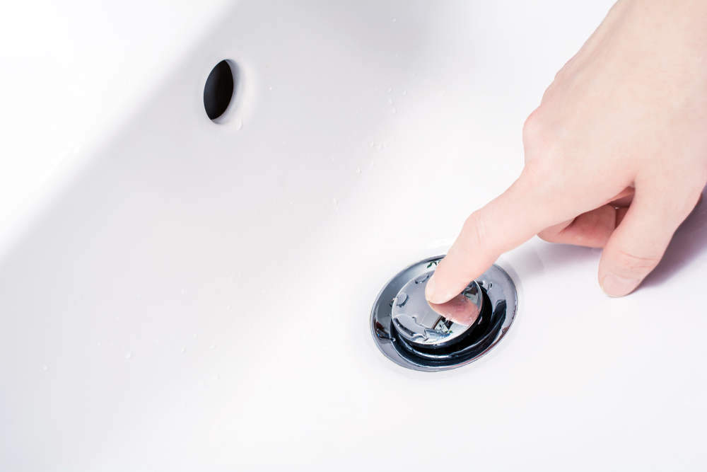 Finger pressing a chrome sink drain plug against white porcelain