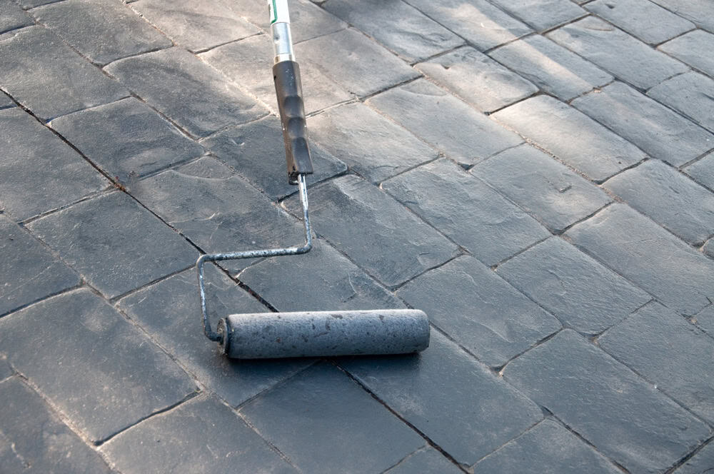 A paint roller rests on freshly sealed stone pavers, showcasing the start of a DIY home improvement project.