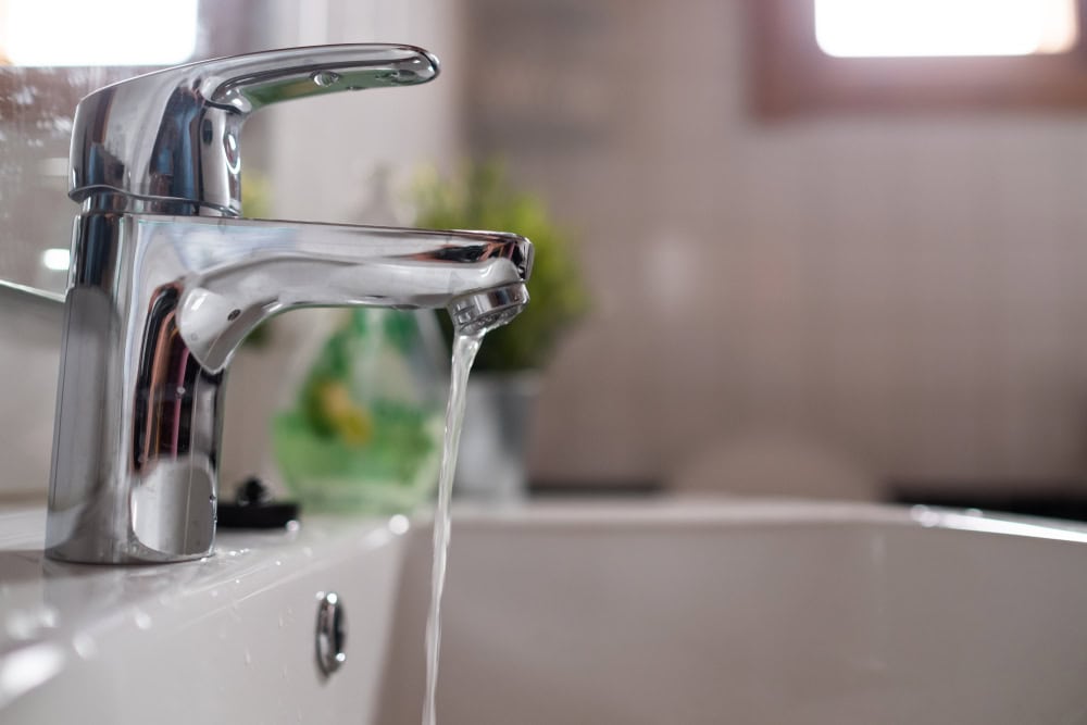 Crystal-clear water flows from a sleek chrome faucet, bringing life to a serene bathroom setting.