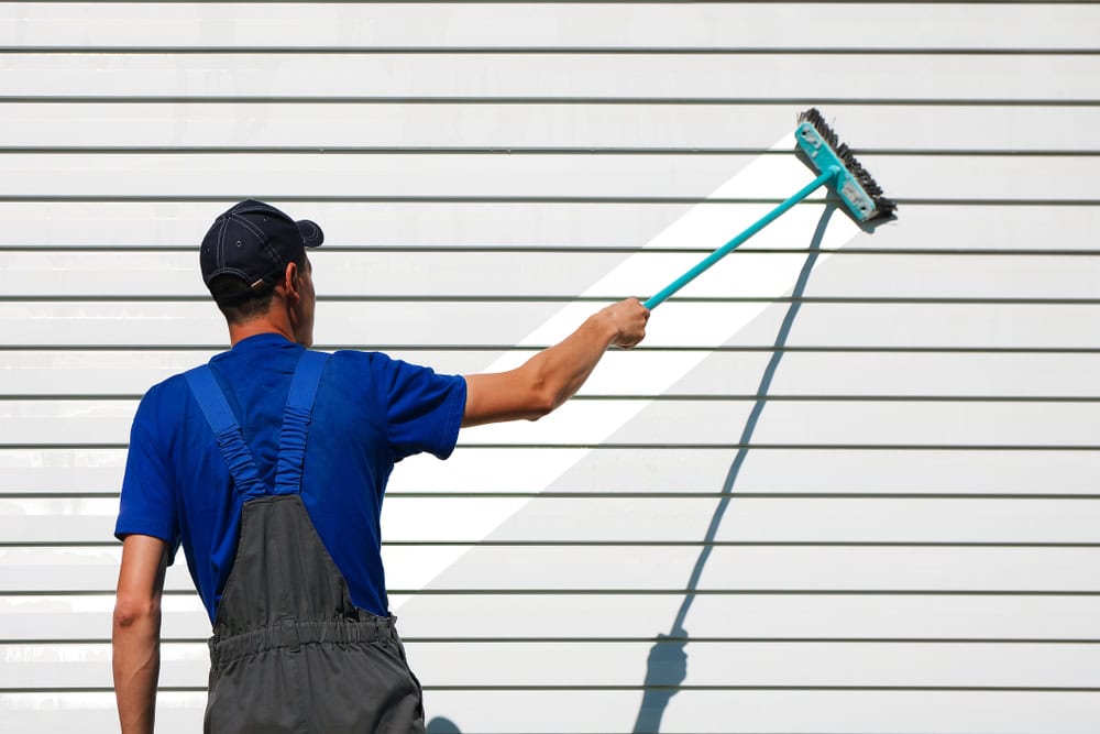A worker diligently cleans the exterior of a building with a long-handled brush.