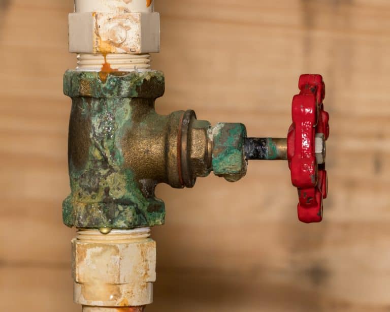 Corroded brass valve with a red handle and signs of leakage, highlighting the effects of oxidation and wear on plumbing.