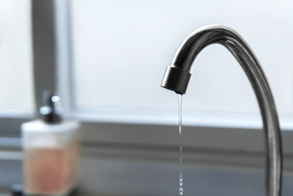 A thin stream of water drips from a curved chrome faucet, capturing the quiet essence of everyday waste.