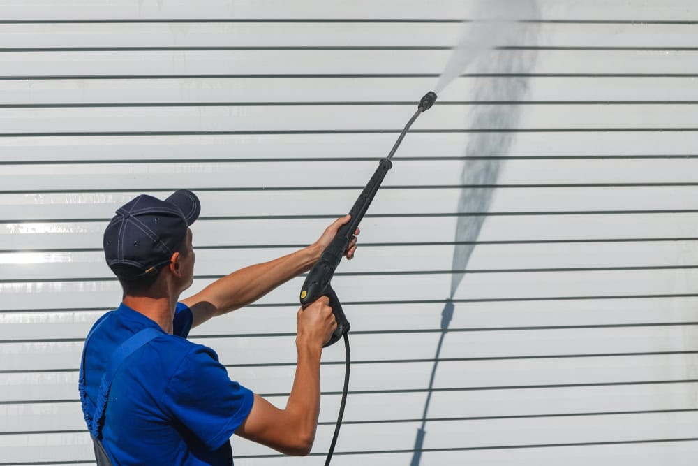A worker power washing a white wall, creating a misty spray.