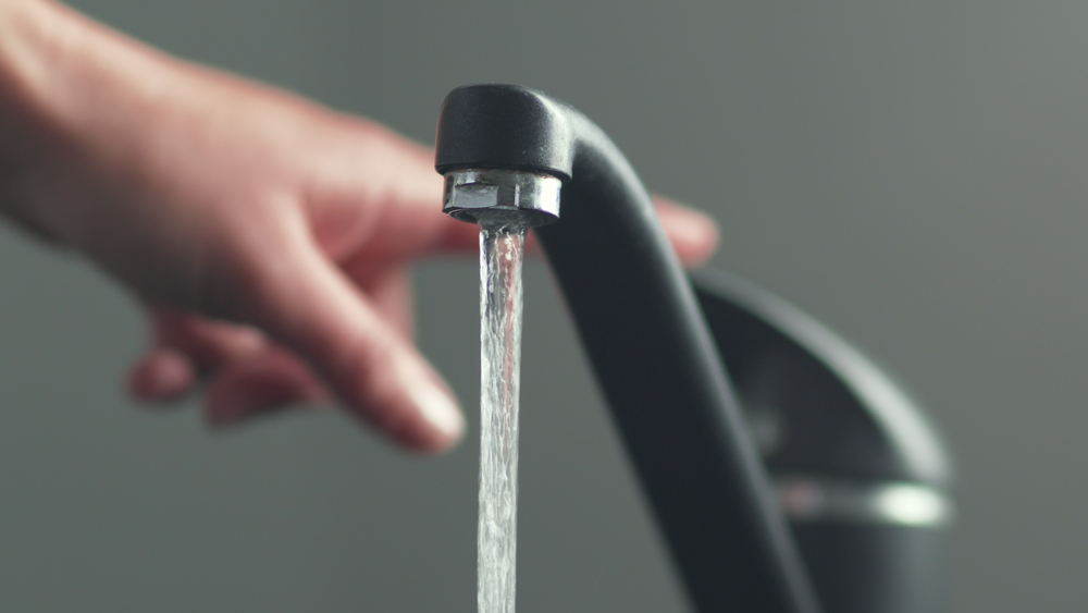 A hand reaching towards a stream of water flowing from a modern black faucet.