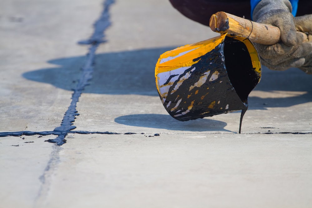 Worker sealing concrete joints with hot tar to prevent cracks and water damage.