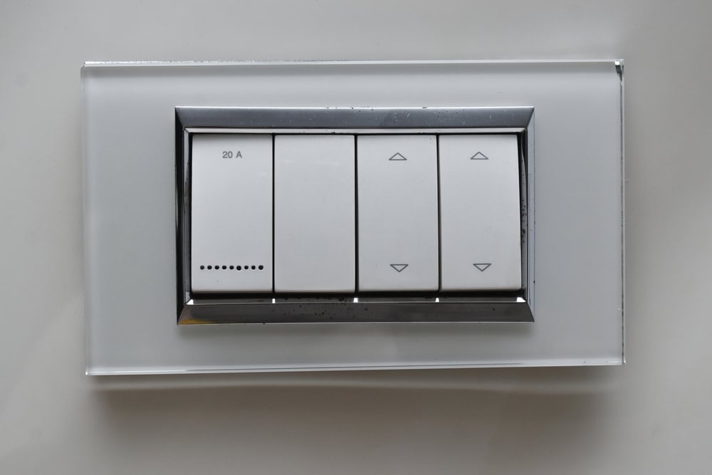 Modern light switch panel with four white buttons, mounted on a sleek gray wall, featuring up/down controls and a 20A rating.