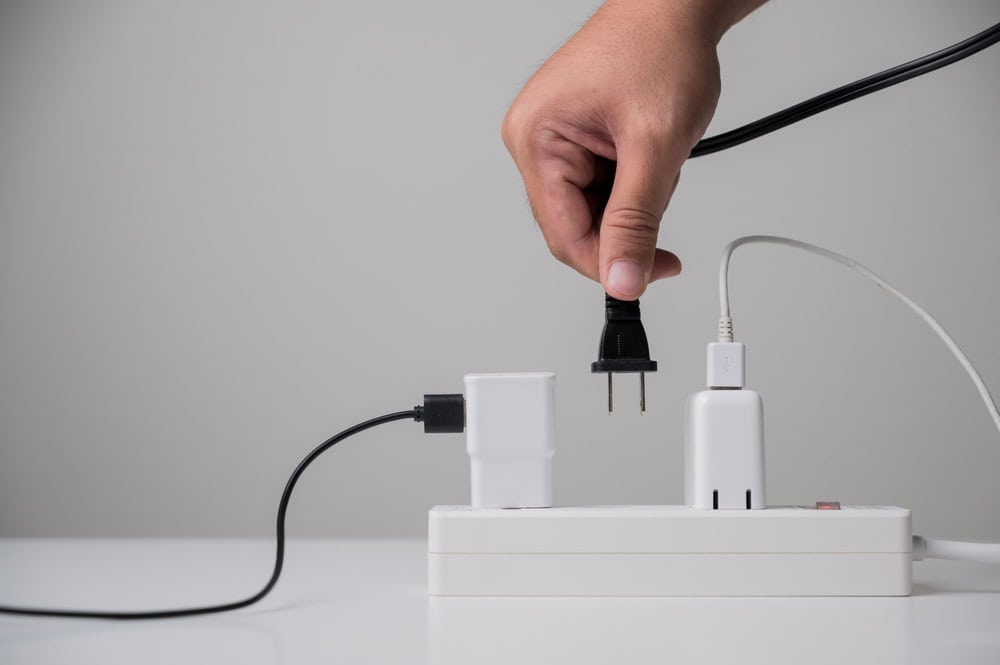 Powering up: A hand plugs a black cord into a white power strip already charging electronic devices.