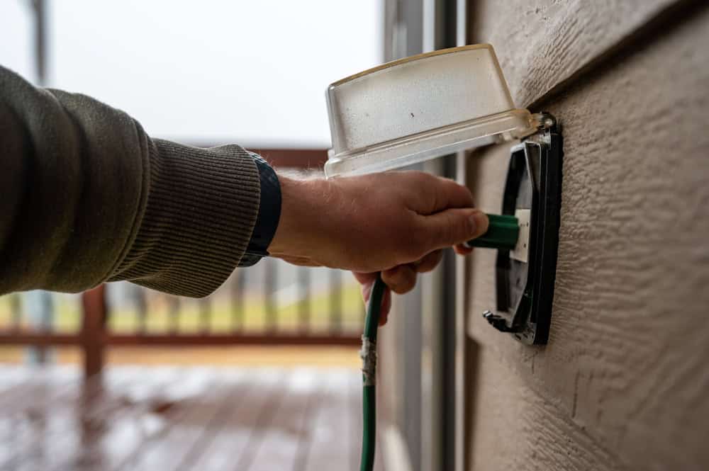 Man plugging in green extension cord outside.