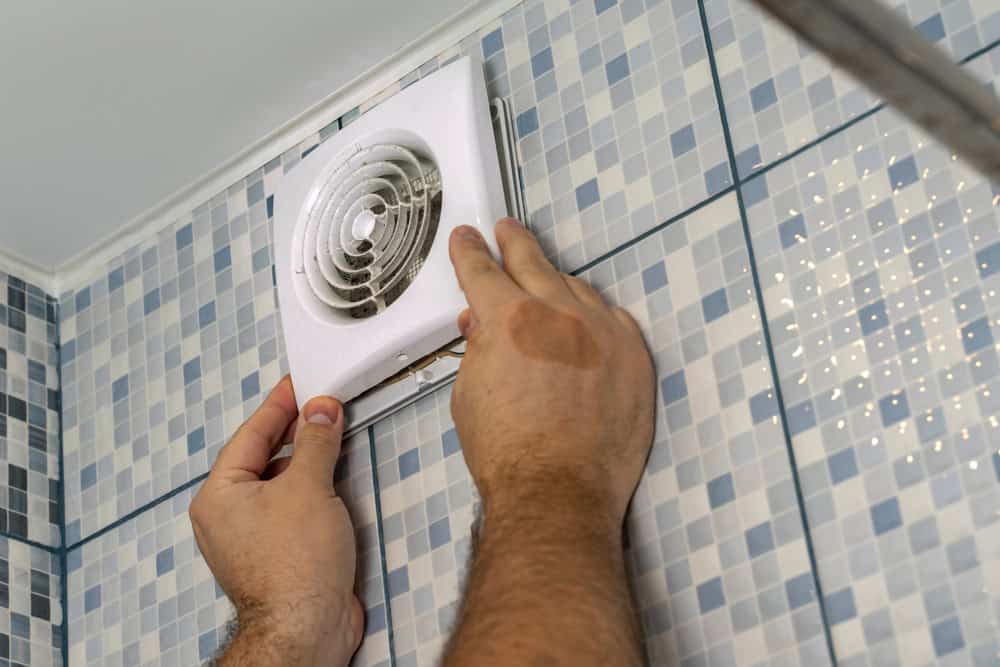 Installing a bathroom exhaust fan on a blue and white tiled wall