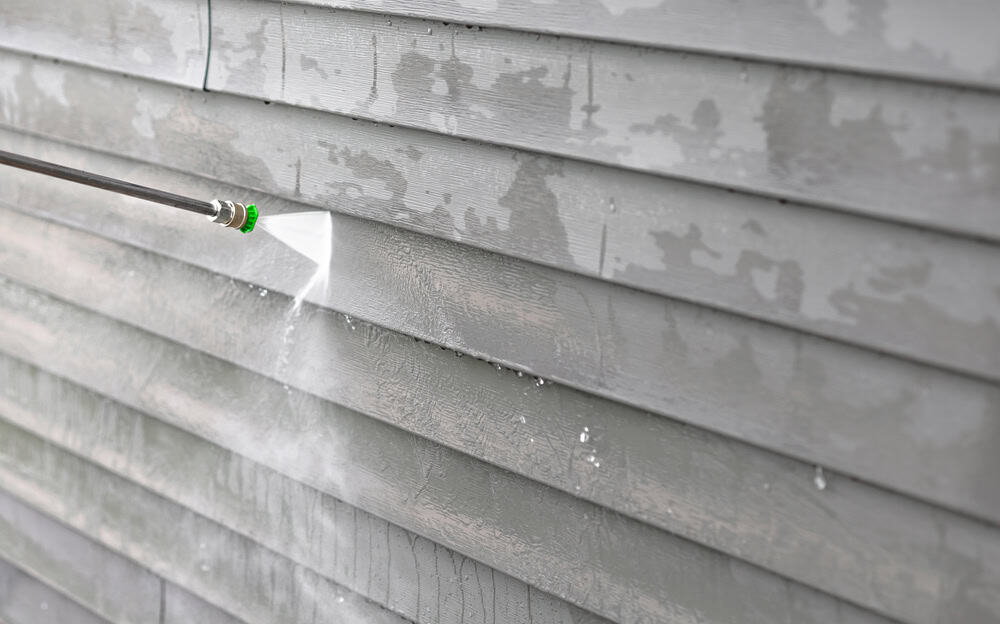 Power washing old paint off a house exterior, revealing a clean surface beneath.