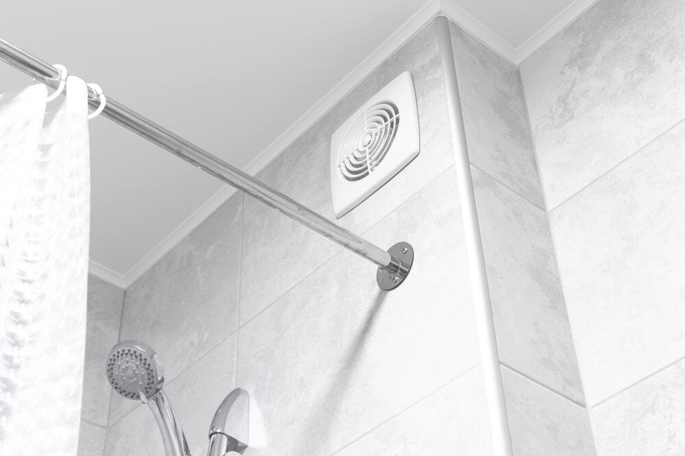Modern bathroom corner with a showerhead, ventilation fan, and gray tiles.