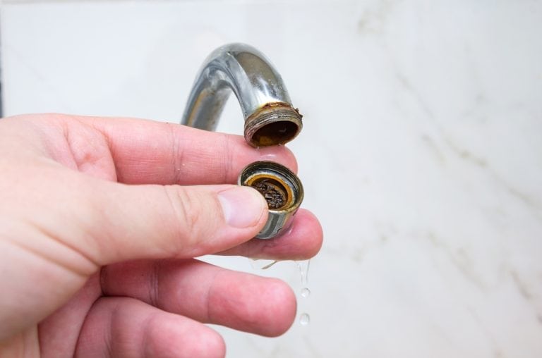 Clogged faucet aerator being removed for cleaning due to rust and sediment buildup.