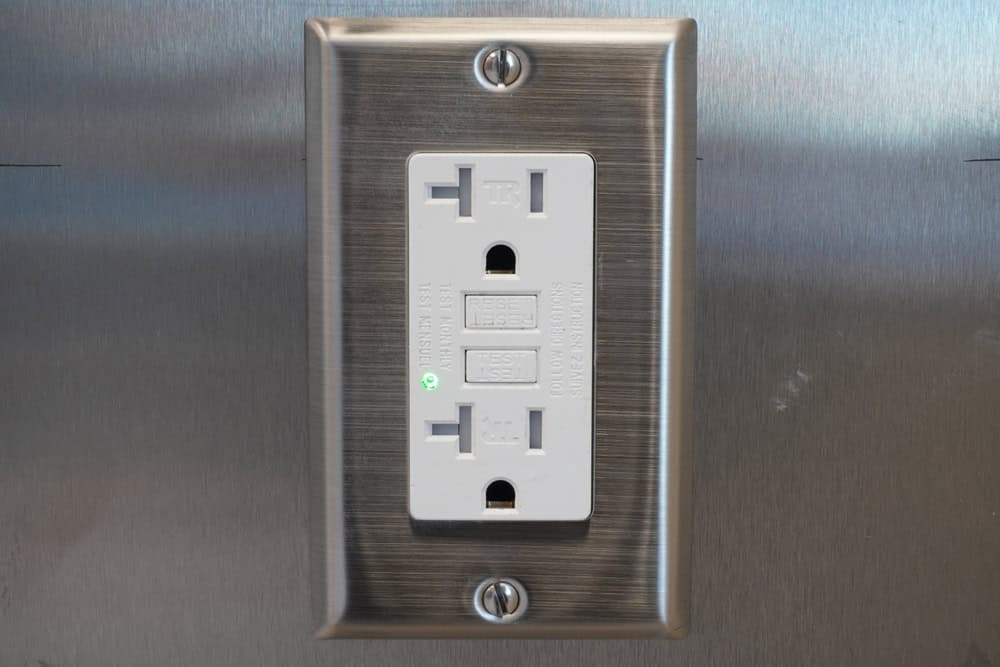 GFCI outlet with a stainless steel cover plate and green indicator light.
