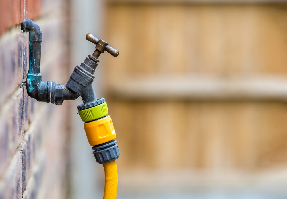 Old metal outdoor tap with bright yellow garden hose connector mounted on brick wall